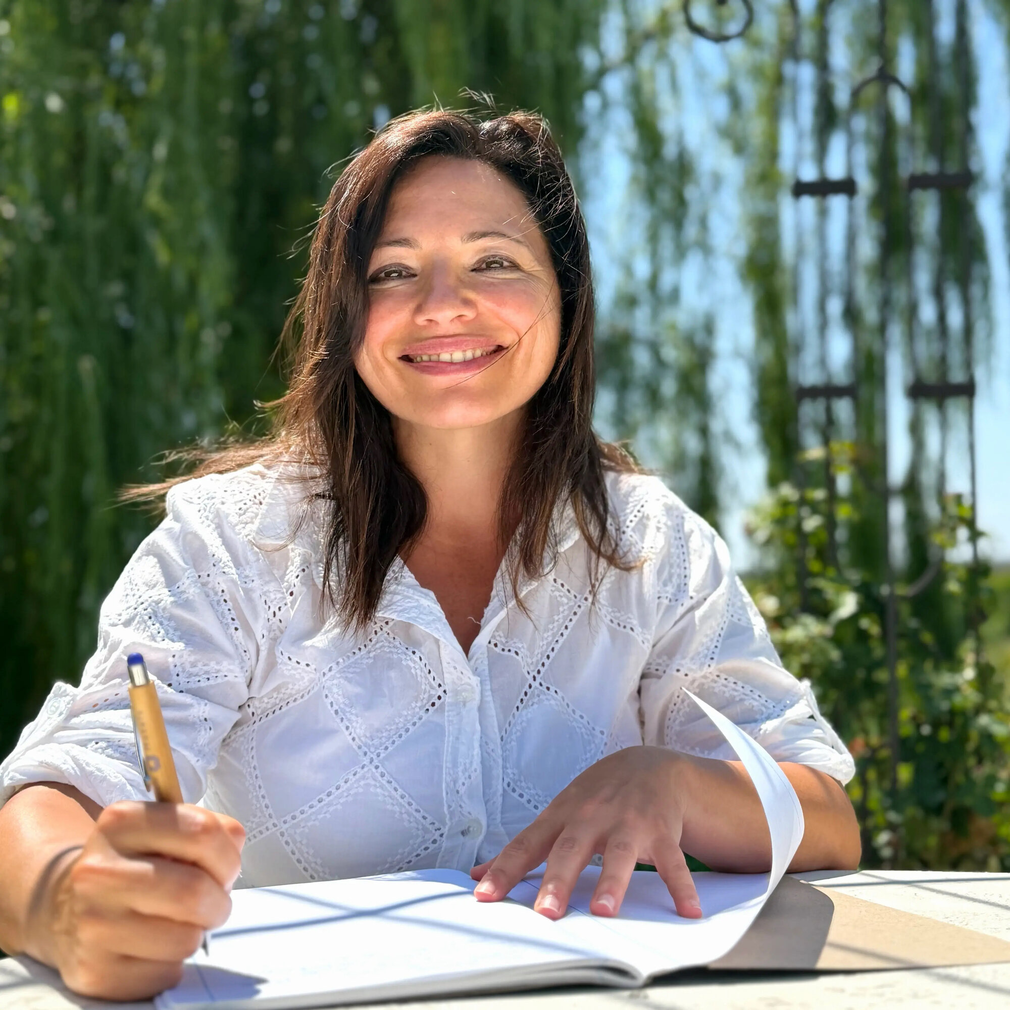 Silvia sorride con la penna in mano sul quaderno aperto, nella luce del giardino